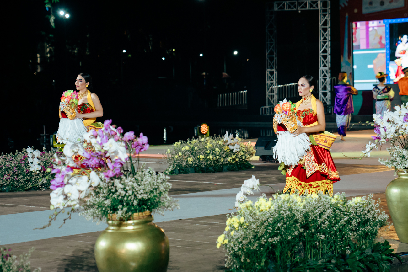 2 girls wearing traditional Banyuwangi costumes, walking down a runway holding their head pieces in preparation to dance